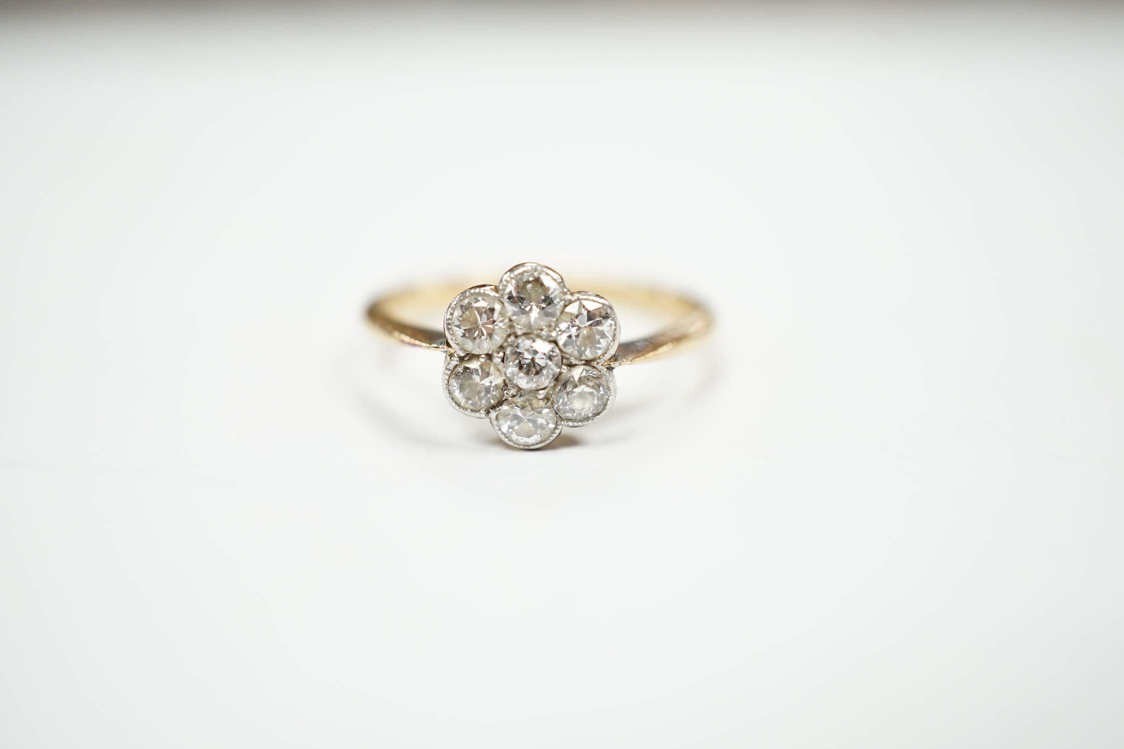 An 18ct and seven stone diamond set flower head cluster ring, size M/N, gross weight 2.9 grams.